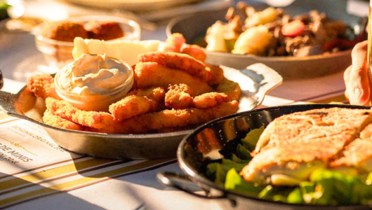 Plates of fried food and salad on a sunlit table.