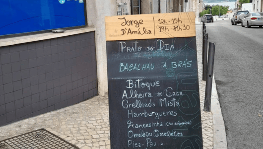 Chalkboard menu outside restaurant, listing daily specials and hours in Portuguese.