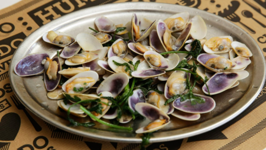 Plate of clams with herbs on a patterned surface.