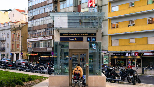 Person in wheelchair entering glass elevator on urban street.