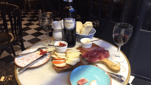 Table with wine, bread, cheese, prosciutto and apple slices on plates.
