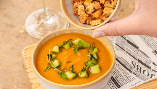 Bowl of soup garnished with herbs and croutons being poured from a cup.