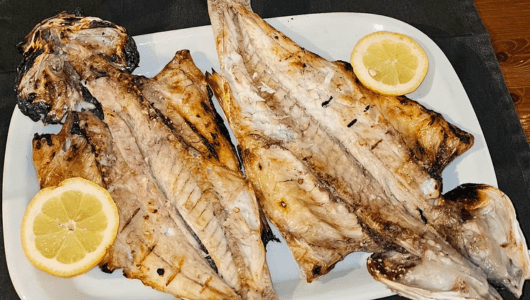 Grilled fish served on a plate with lemon slices.