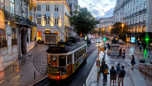 Nighttime city street scene with a yellow tram and people walking.