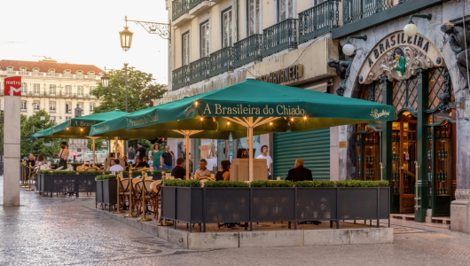 Outdoor café in Lisbon with green umbrellas and people seated at tables.