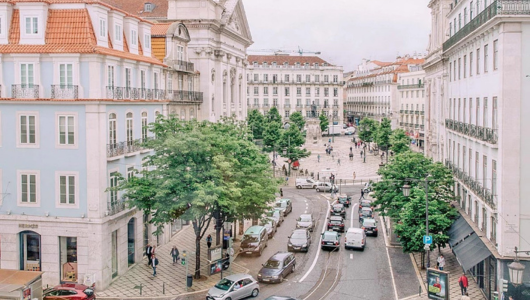 Street view of a European city with cars, people, and historic buildings.