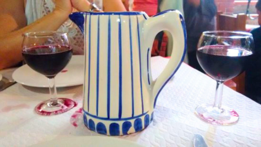Blue-striped ceramic jug and two glasses of red wine on a table.