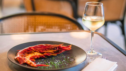 Plate with shrimp and herbs, glass of white wine on table.