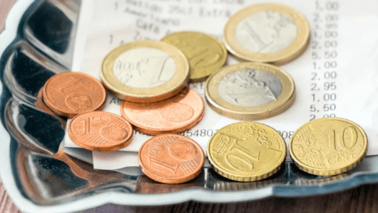 Various Euro coins on a receipt in a metal tray.