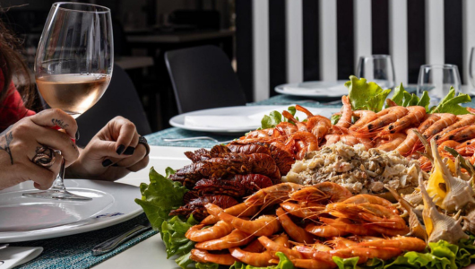 Person holding wine near platter of various seafood and lettuce.