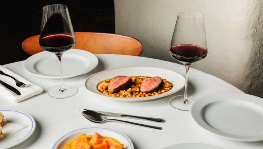 Dining table with wine, meat on beans, and fruit dessert.