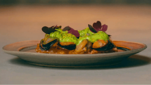 Gourmet dish with mussels, green sauce, and garnish on a plate.