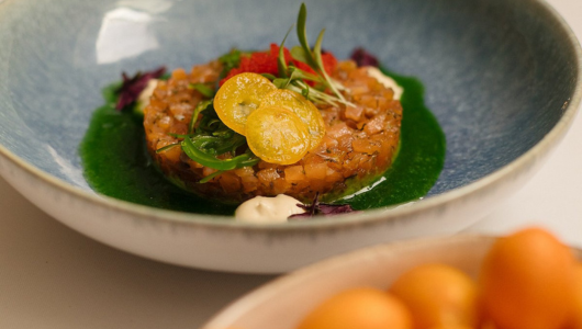 Gourmet dish with diced salmon tartare, herbs, and sauce in a blue bowl.