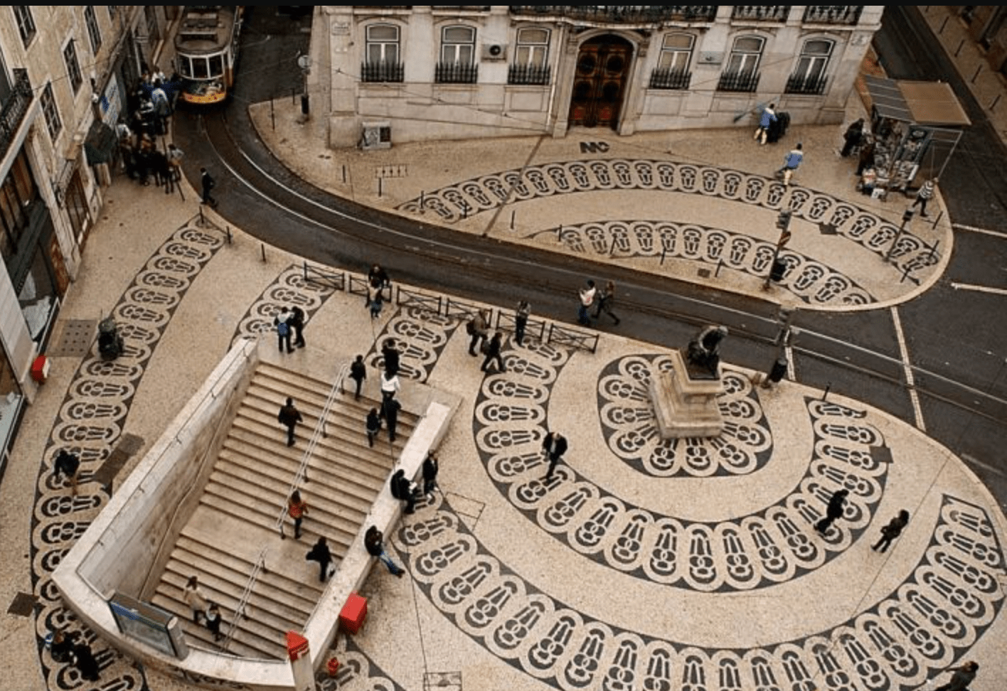 Aerial view of patterned cobblestone street with people and a tram in Lisbon.