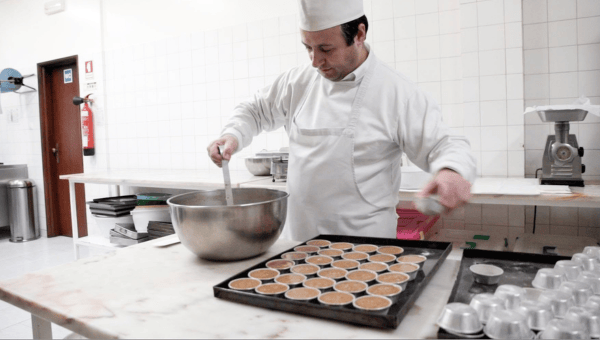 Chef in white uniform mixing batter beside a tray of pastries.