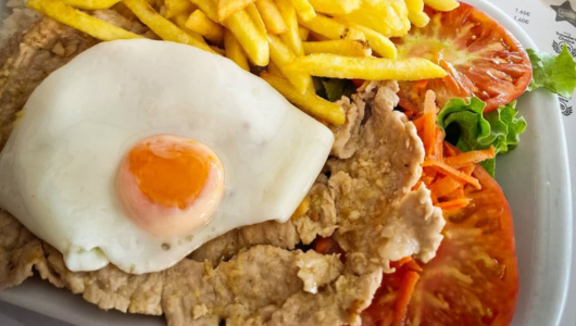 Plate with fried egg, fries, sliced tomato, lettuce, and cooked meat.