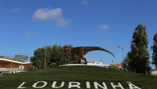 Dinosaur statue on grass hill with 'LOURINHÃ' text, trees, and clear sky.