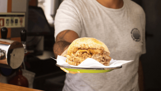 Person in a white shirt holding a sandwich on a paper napkin.