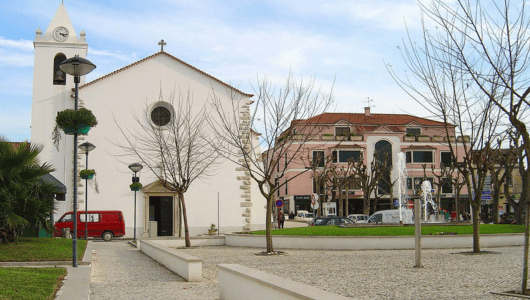 Church and building in a plaza with bare trees and a red van.