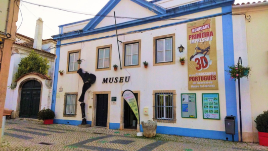 Exterior of a small museum with blue trim and posters in front.