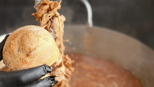 Gloved hand putting beef in bread over stew pot.