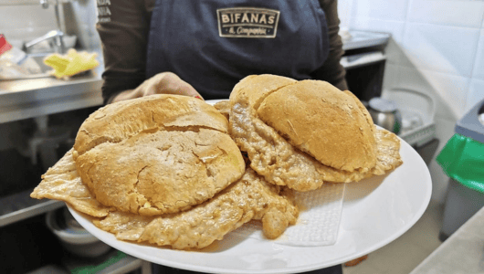 Person holding a plate with two meat-filled sandwiches in a kitchen.