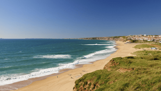 Coastal landscape with sandy beach, blue sea, and clear sky.