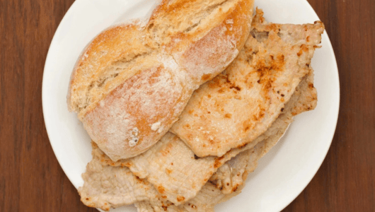 Plate with a sandwich of sliced grilled meat and a crusty baguette.