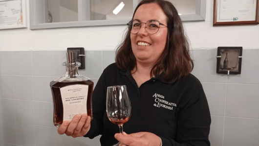 Woman holding a glass and a bottle of brown liquid, smiling indoors.