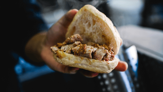 Hand holding a sandwich filled with cooked meat.