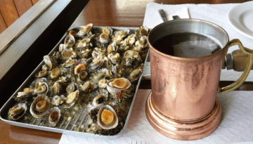 Tray of cooked shellfish and a copper mug with drink on a table.