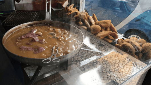 Pan with stew and breaded food on a street food stall.