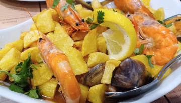 Dish with shrimp, clams, fried potatoes, lemon slices, and parsley.