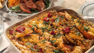 Baked seafood dish with vegetables and rice next to a plate of salad.