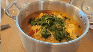 Pot with hearty stew topped with herbs on a table.
