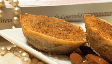Two almond tarts on a plate with scattered almonds and a pearl necklace.