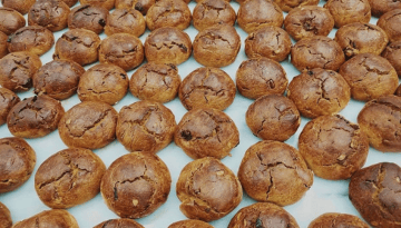 Rows of round, brown pastries with cracked tops on a light surface.