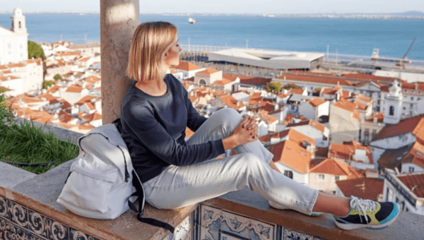 Woman sitting on ledge overlooking cityscape and sea.