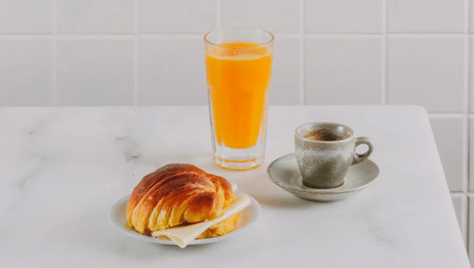Croissant, orange juice, and espresso on a white table.