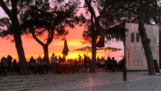 Silhouetted crowd at a cafe sunset with trees and umbrellas.