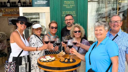 Group of people smiling and toasting with wine outside a shop.