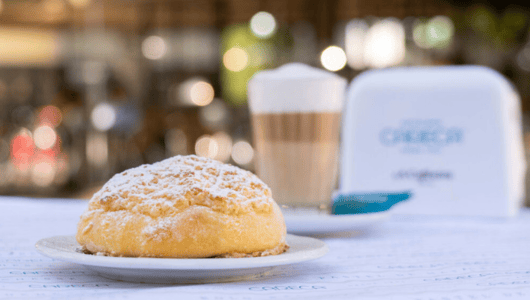 Pastry with powdered sugar, latte in background on a table.