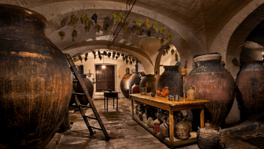 Historic cellar with large clay pots, wooden table, and hanging herbs.