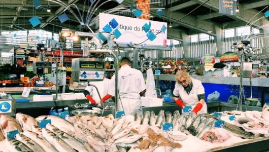 Fish market stall with two workers arranging seafood under bright lighting.