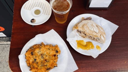 Table with beer, sandwich, fritter, and mustard.