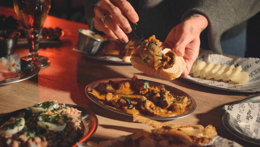 Person serving curry onto bread at a table with various dishes.