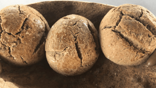 Three round, rustic bread rolls in a wooden bowl.