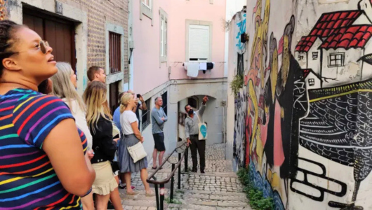 People view mural art on walls of narrow cobblestone alley.