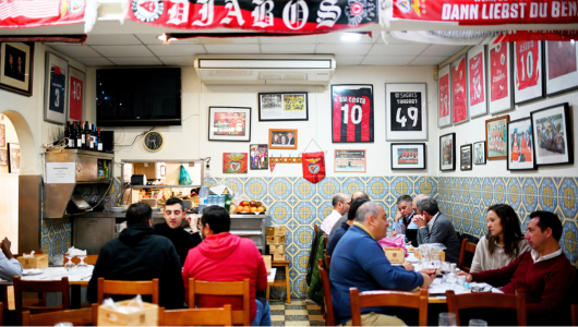 People dining in a sports-themed restaurant with jerseys and scarves on the walls.