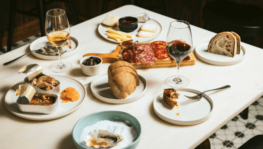 Table with wine, bread, cheese, charcuterie, and canned seafood.